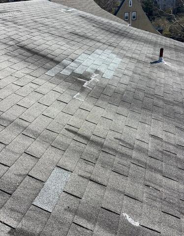 Worn gray shingle roof with visible damage and patching before roofing work
